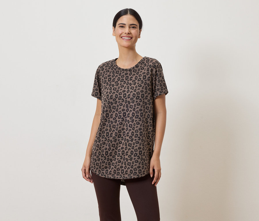 Une femme aux cheveux relevés porte un t-shirt marron à motif léopard et un legging marron sur un fond clair.