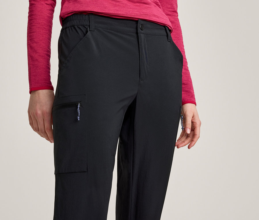 Gros plan d'une personne portant un pantalon noir avec une poche cargo zippée sur la cuisse gauche et un haut rouge à manches longues.