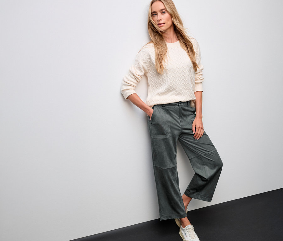 Femme posant en pull crème et pantalon de velours vert Straight Leg Street One contre un mur.