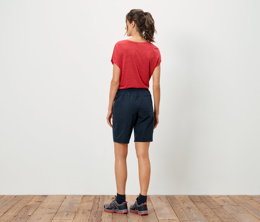 Vue arrière d'une femme portant un t-shirt rouge et un short bleu debout sur un plancher en bois.