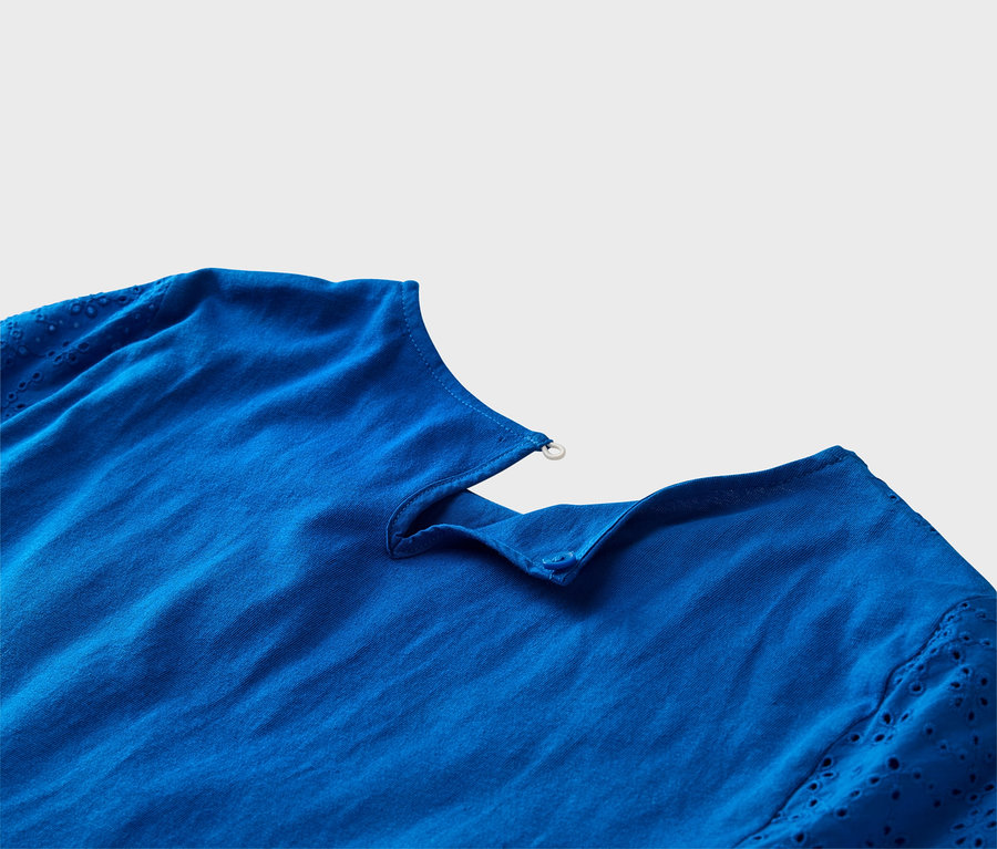 Gros plan d'un haut bleu cobalt avec des manches en broderie anglaise et des détails de boutons.
