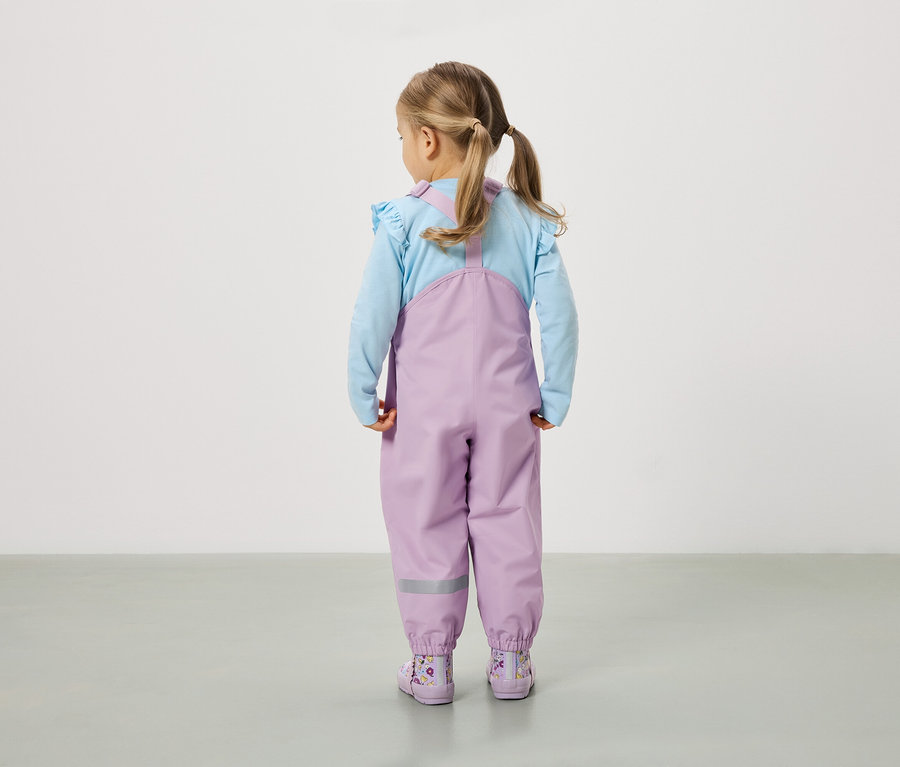 Une fillette avec des couettes se tient dos à la caméra, portant un pantalon violet et des bottes assorties.