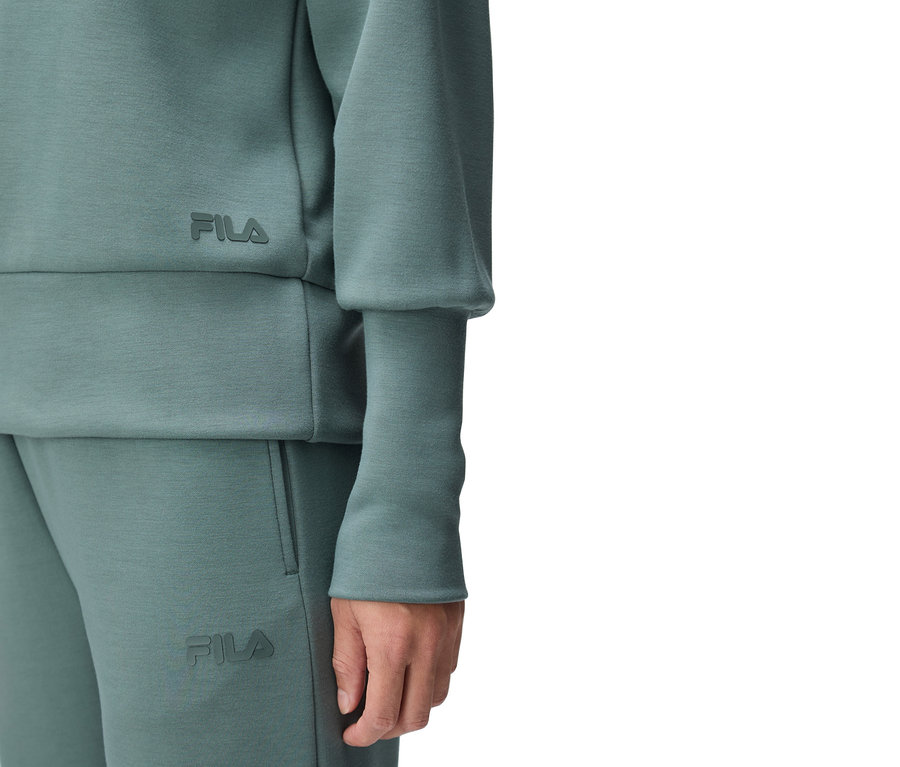 Gros plan d'une personne portant un survêtement Fila turquoise, avec le logo Fila visible sur le haut et le pantalon.