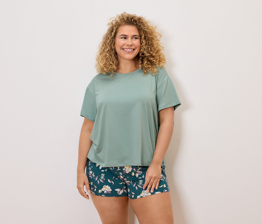 Femme aux cheveux bouclés, portant un t-shirt vert et un short à fleurs.