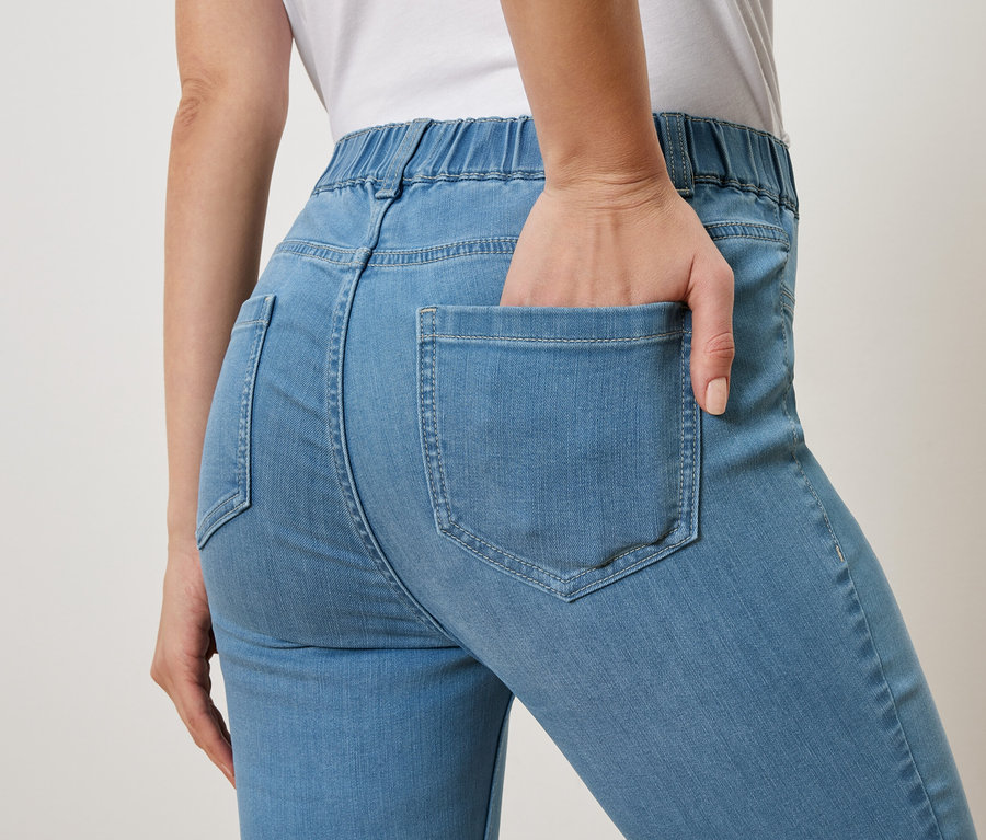 Femme avec la main dans la poche arrière d'un jean bleu clair.