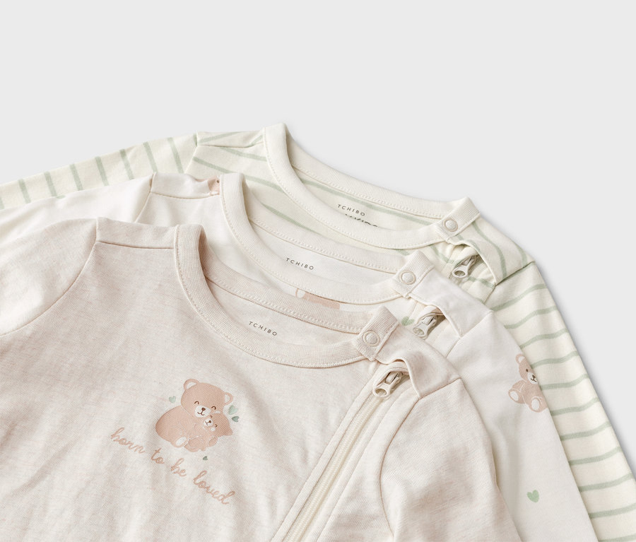 Trois pyjamas pour bébé sont superposés, l'un avec un motif d'ours et l'inscription "born to be loved", l'un avec un motif d'ours et des rayures vertes.