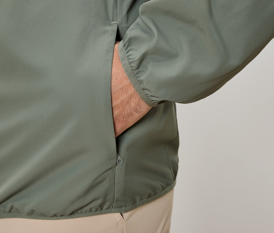 Gros plan d'une personne qui met la main dans la poche d'une veste vert olive.