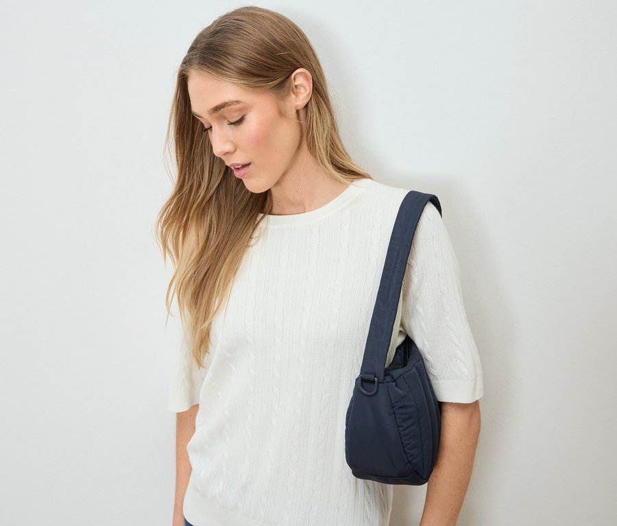 Femme blonde portant un pull blanc avec un sac à main bleu marine sur l'épaule.