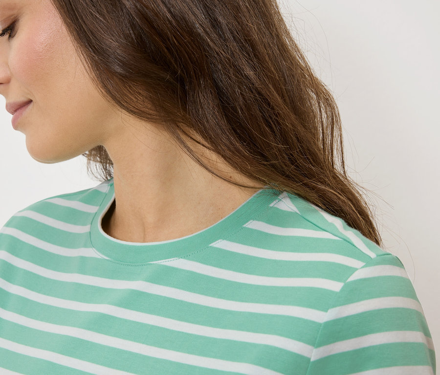 Gros plan d'une femme aux cheveux bruns portant un t-shirt rayé vert et blanc.