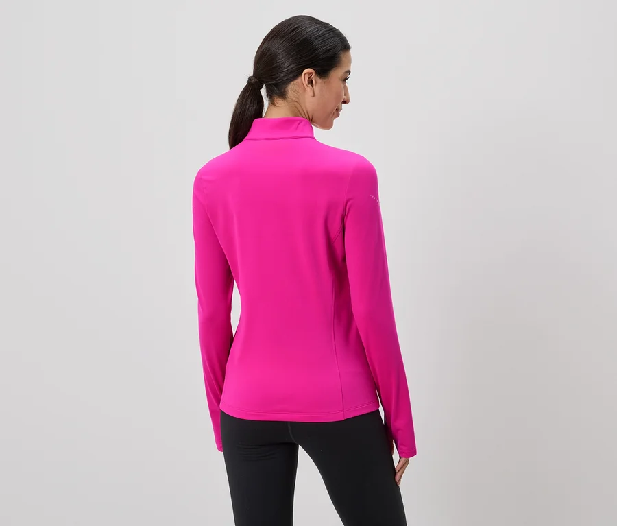 Une femme vue de dos, avec une queue de cheval, porte un haut rose à manches longues et un legging noir sur un fond gris.