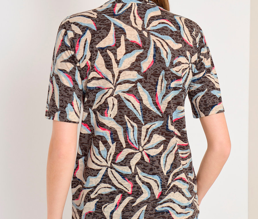 Femme de dos portant un t-shirt manches courtes CECIL à motif foncé avec des formes de feuilles claires, bleues et roses, et un jean bleu.