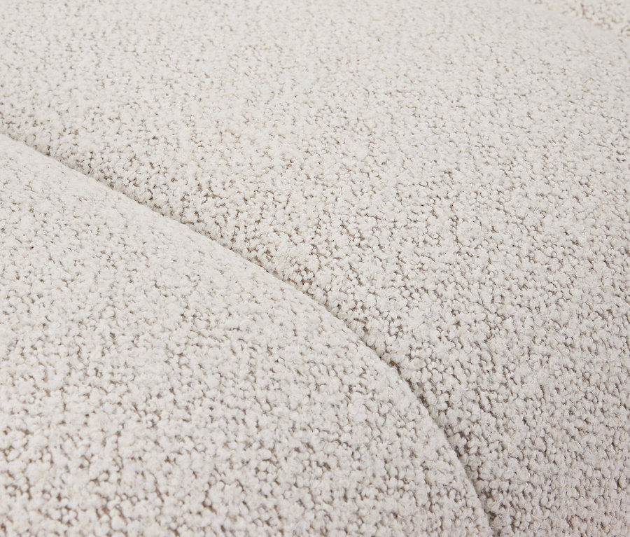 Gros plan d'un canapé crème en tissu bouclé avec une douce courbe.