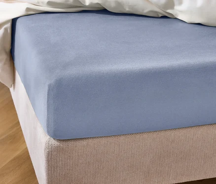 Gros plan d'un lit avec un drap-housse bleu clair et une bordure de lit beige sous une couverture blanche.