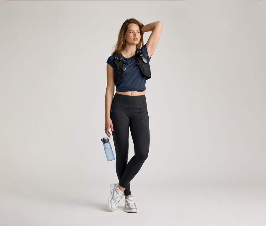 Femme en leggings d’extérieur, t-shirt bleu et gilet de course posant avec une bouteille d'eau et la main sur la tête.