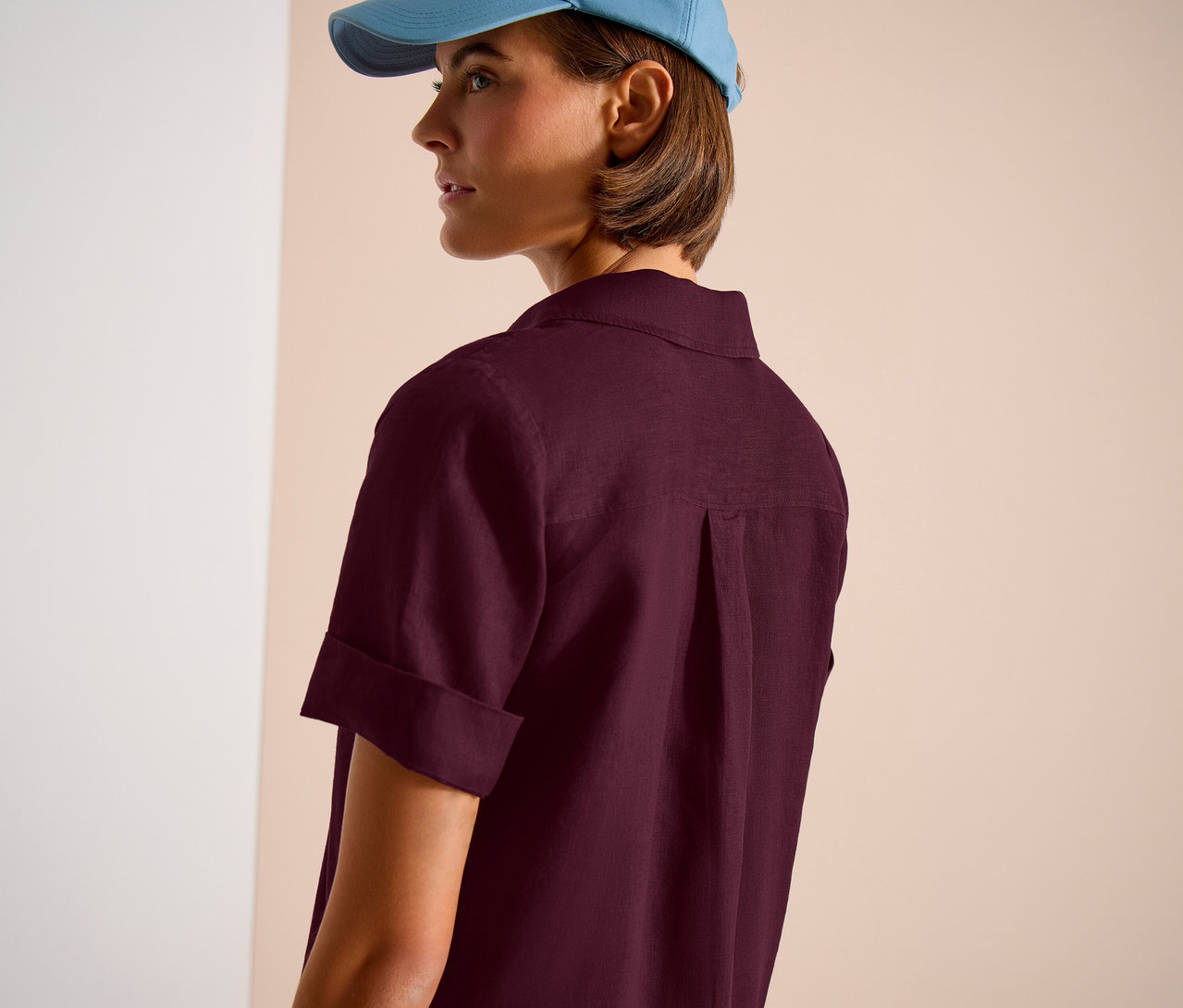 Femme portant une casquette bleu clair et une chemise bordeaux, vue de dos.