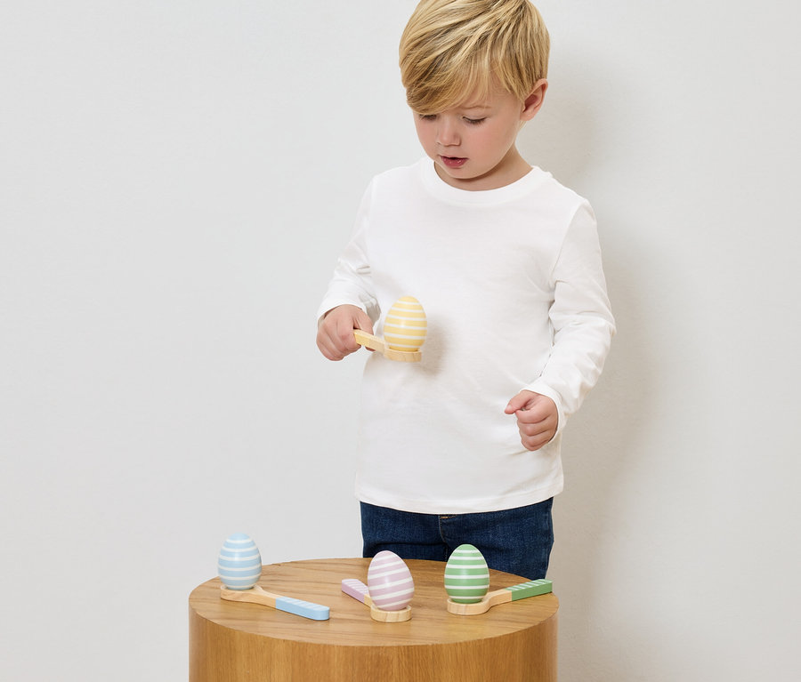Un garçon joue avec des œufs en bois peints et de petits marteaux sur une table en bois.