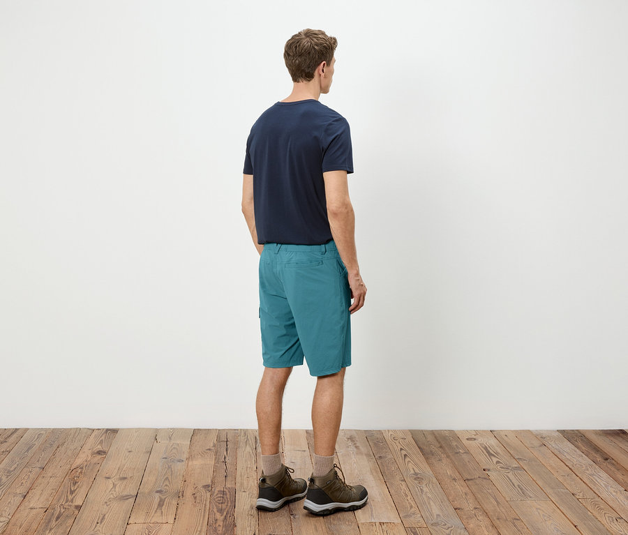 Homme vu de dos, portant un t-shirt bleu, un short turquoise et des chaussures de randonnée.