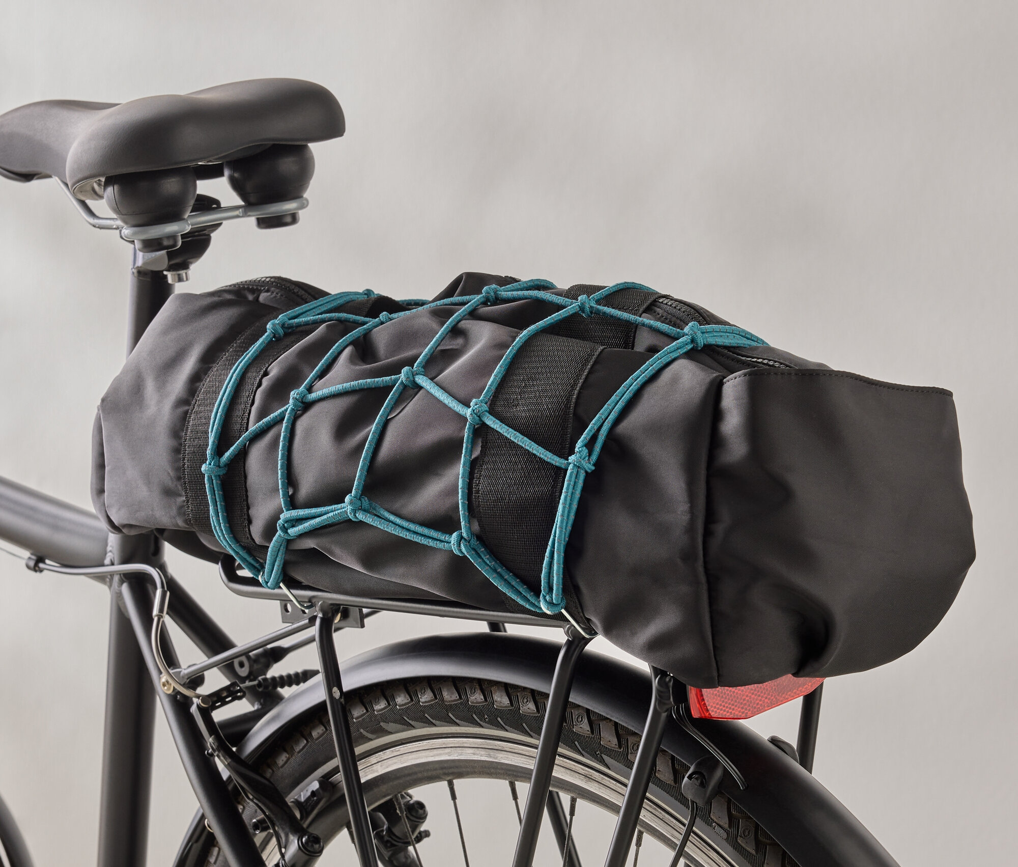 Un sac de vélo noir est fixé à un porte-bagages de vélo noir à l'aide d'un filet à bagages bleu.