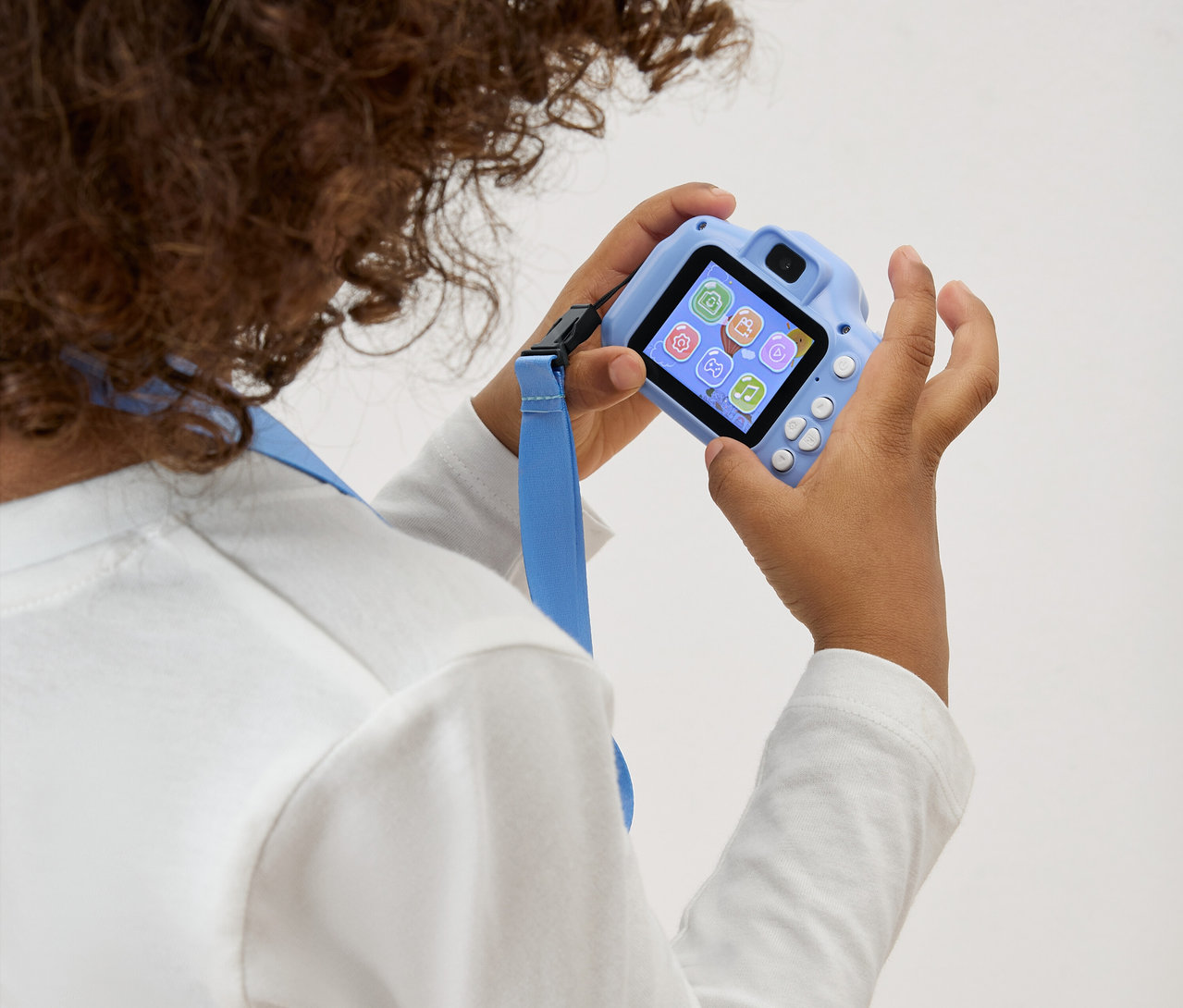 Un enfant tient un appareil photo jouet bleu clair avec une dragonne bleue devant lui.