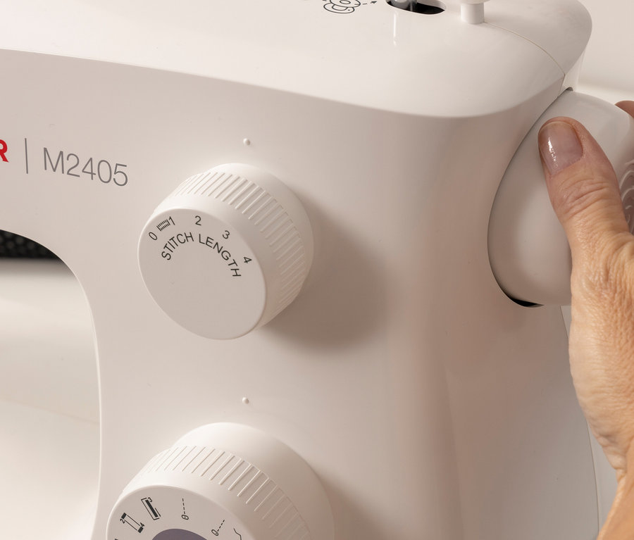 Une main ajuste le bouton de longueur de point sur une machine à coudre Singer «
M2405
».