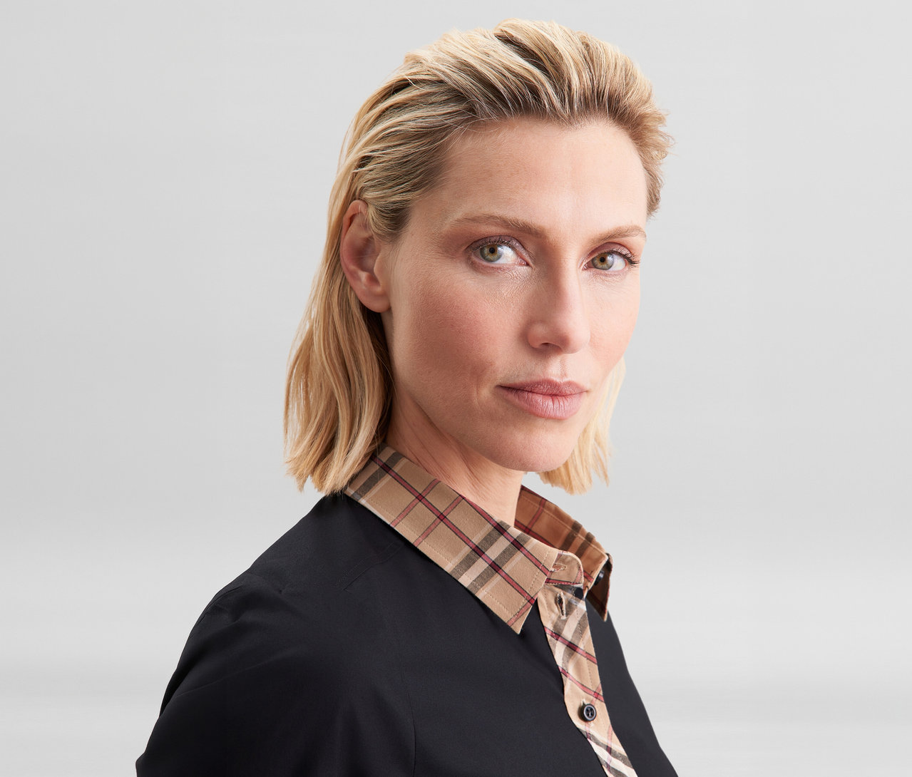 Femme blonde portant un chemisier en popeline à carreaux Seidensticker noir avec un col et une patte de boutonnage à carreaux beiges, rouges et noirs.