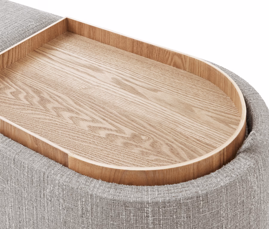 Gros plan d'un plateau en bois clair aux coins arrondis, inséré dans un meuble rembourré gris texturé.