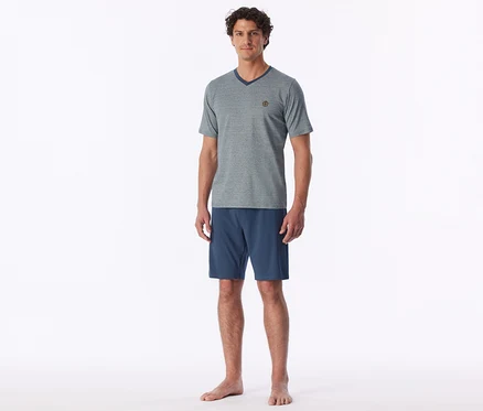 Un homme debout pieds nus, portant un t-shirt gris à col en V et un short bleu.