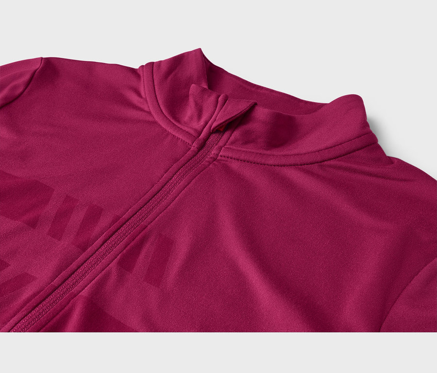Veste magenta avec un col montant et une fermeture éclair partiellement ouverte. Un motif subtil et plus foncé est visible sur le tissu à gauche de la fermeture éclair.