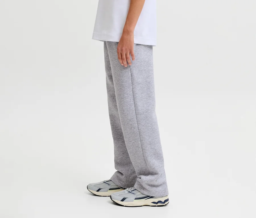 Une personne porte un pantalon de survêtement Jack&Jones Bradley gris et des baskets.