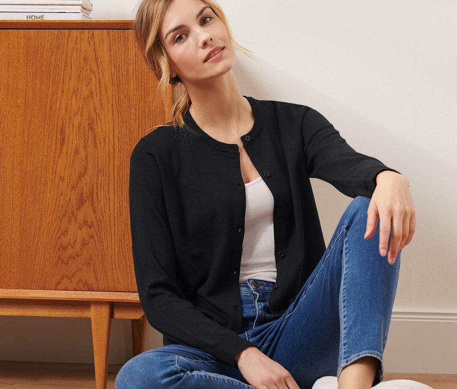 Une femme est assise par terre et porte un cardigan noir en maille fine.