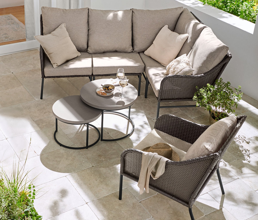 Canapé d'angle avec tressage en polyrotin, fauteuil de salon avec tressage en polyrotin et 2 tables basses avec plateau de table en béton sur une terrasse.