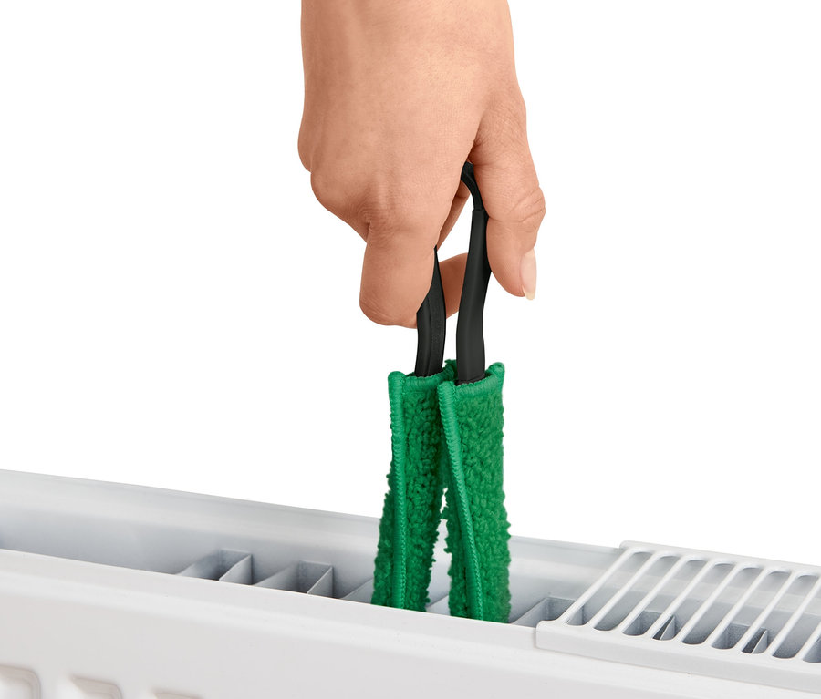 Une main tient une brosse à végétaux sur un radiateur.