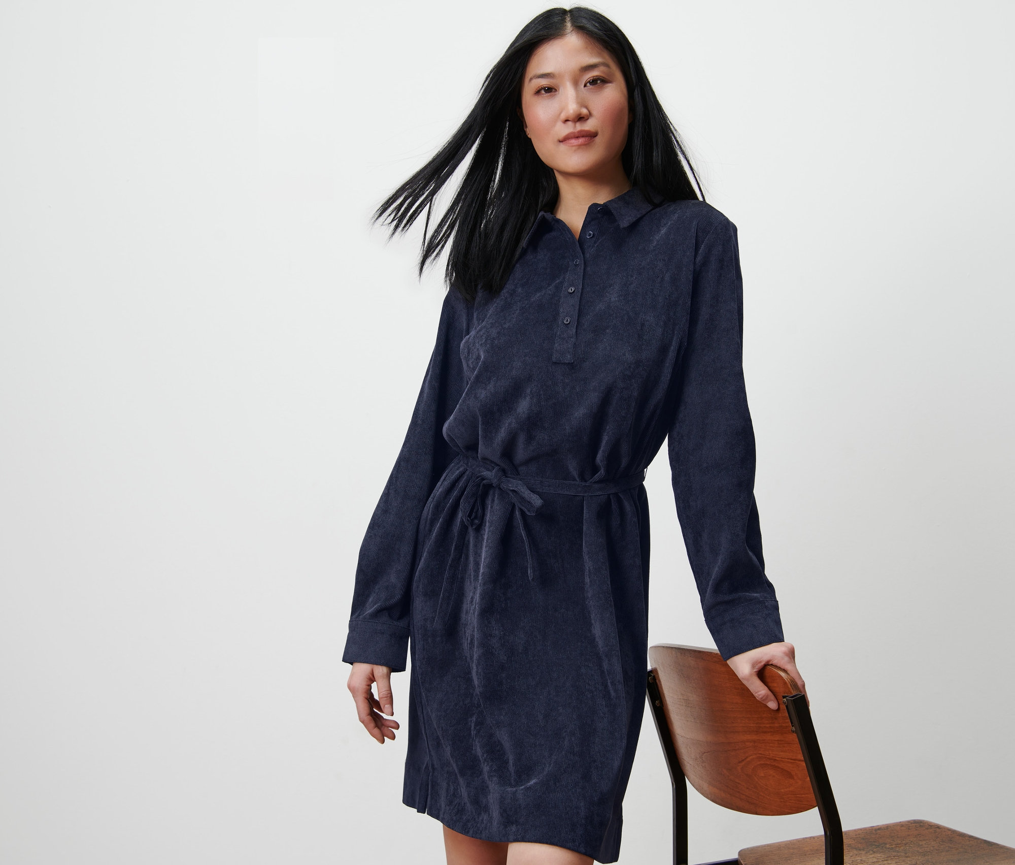 Femme posant en robe en velours côtelé, appuyée sur une chaise.