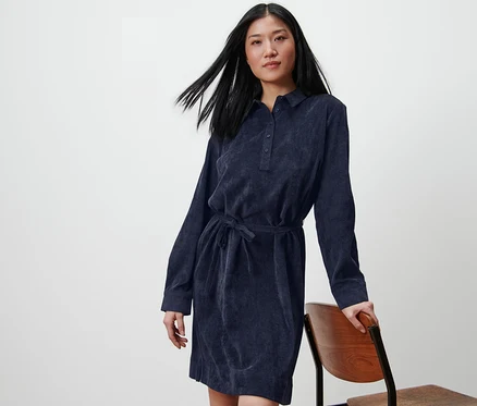 Femme posant en robe en velours côtelé, appuyée sur une chaise.