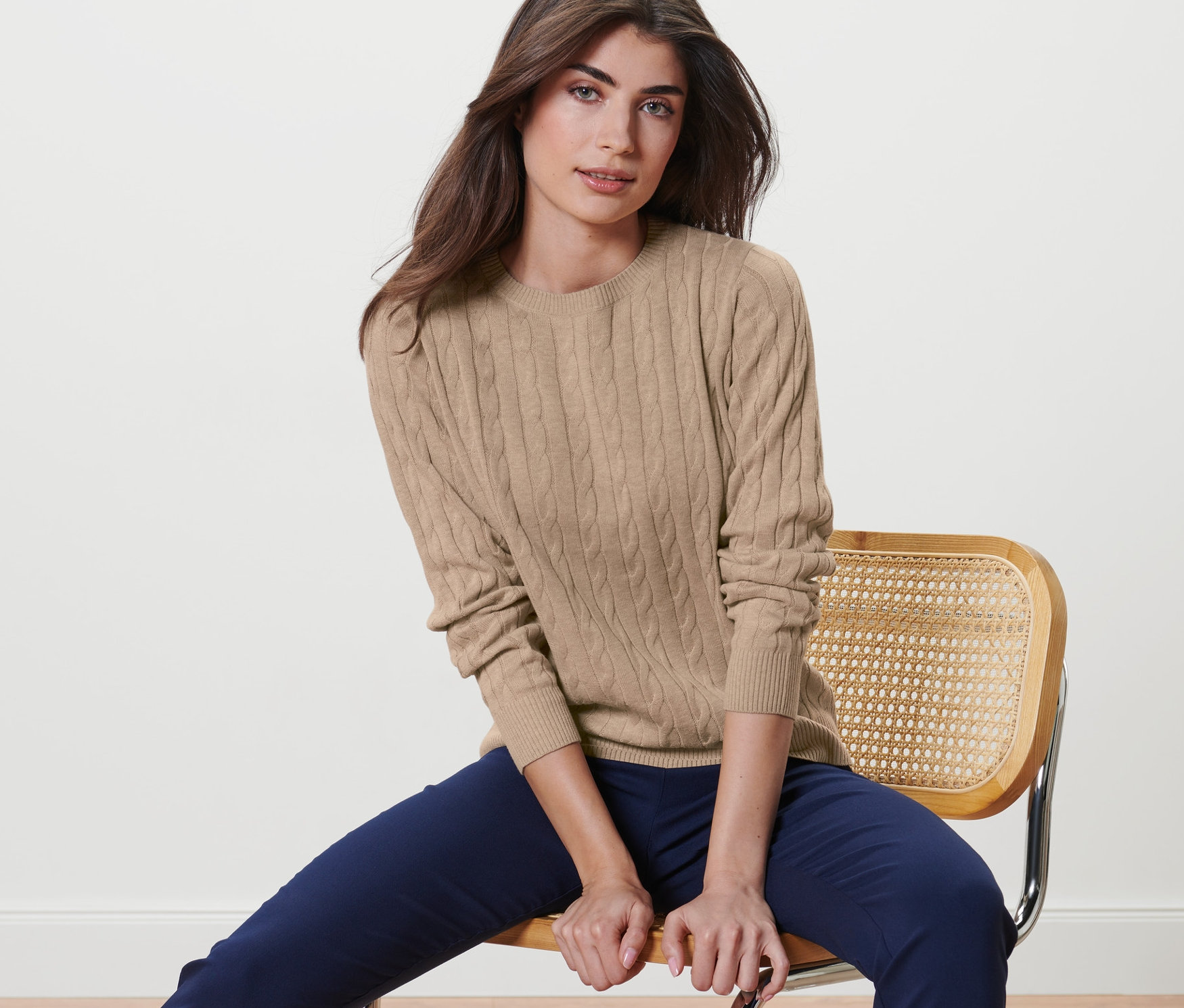 Une femme est assise sur une chaise et porte un pull en maille torsadée crème chiné.