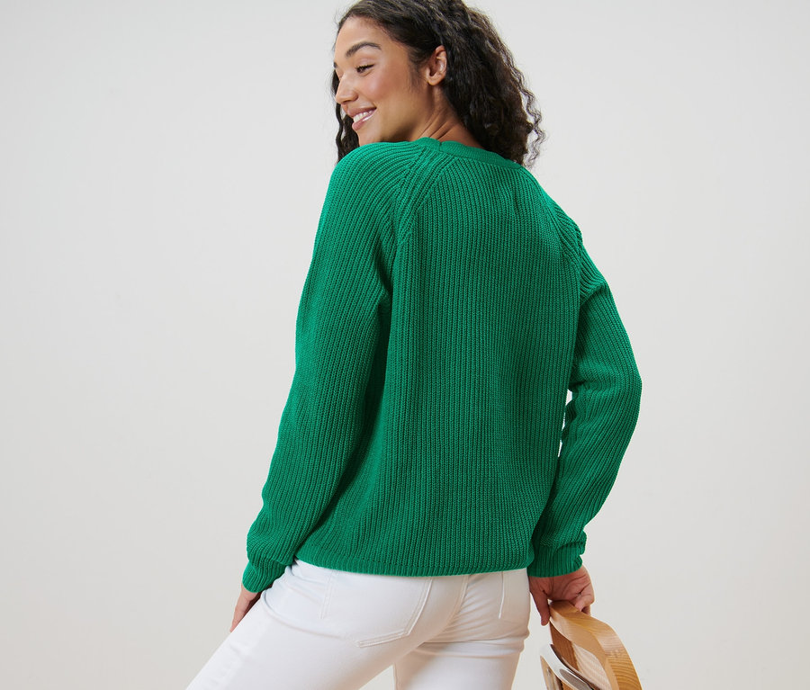 Femme regardant par-dessus son épaule et posant en cardigan vert en grosse maille et jean blanc.