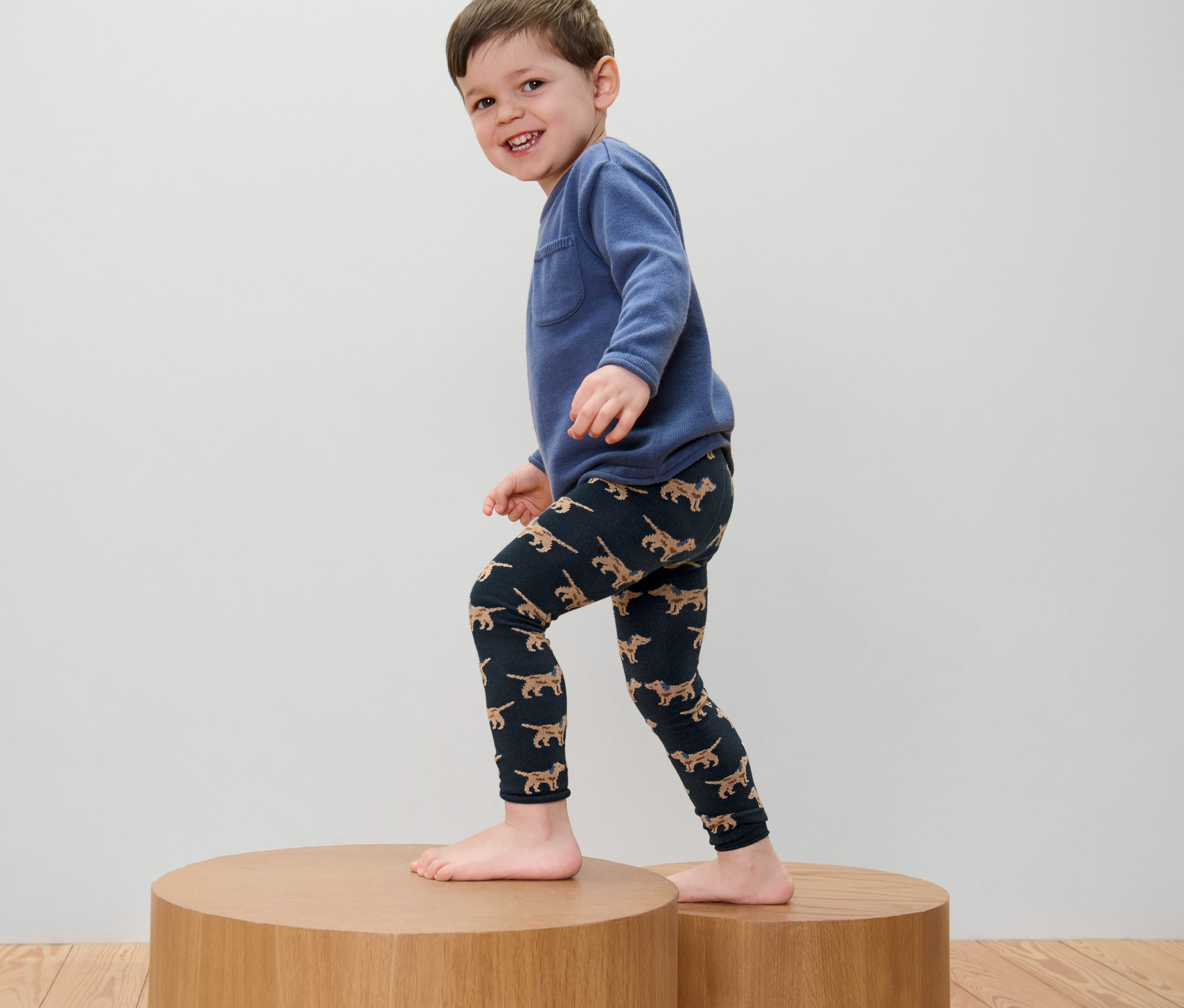 Garçon portant un sweat bleu et 2 leggings en maille pour enfant avec broderie debout sur un piédestal en bois.
