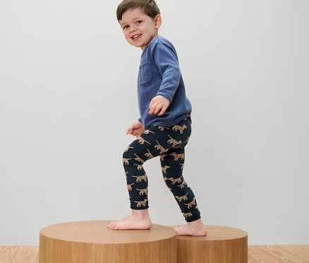 Garçon portant un sweat bleu et 2 leggings en maille pour enfant avec broderie debout sur un piédestal en bois.