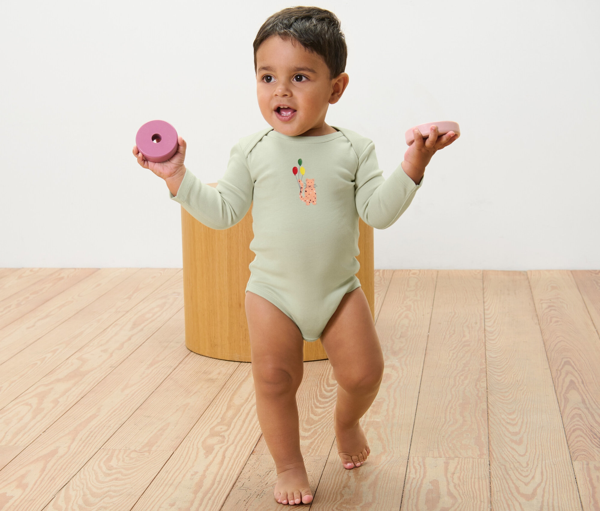 Un bébé portant un body à manches longues avec un imprimé tient un jouet dans chaque main. 5 bodys évolutifs pour bébé