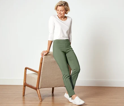 Femme appuyée sur un fauteuil portant un chemisier blanc et un pantalon stretch.