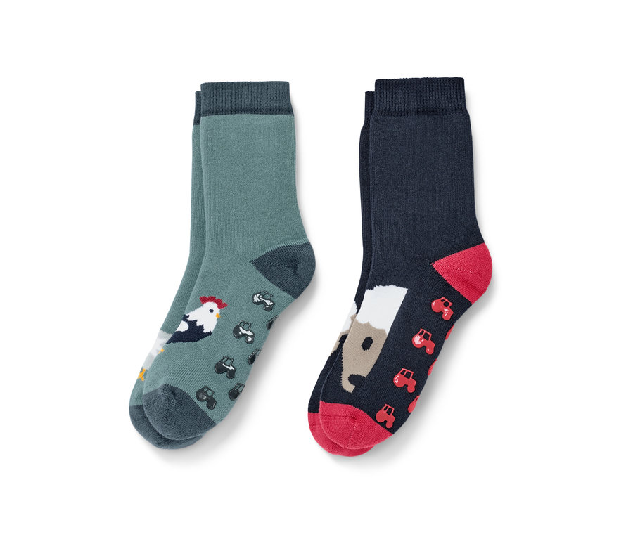 Deux paires de chaussettes antidérapantes pour tout-petit sur le thème de la ferme. Une paire verte avec un coq et des tracteurs, l'autre bleu foncé avec un cheval et des tracteurs.
