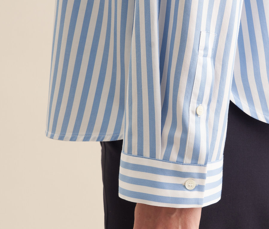 Détail d'une chemise oversize bleue Seidensticker avec des rayures blanches sur le bras d'une femme.