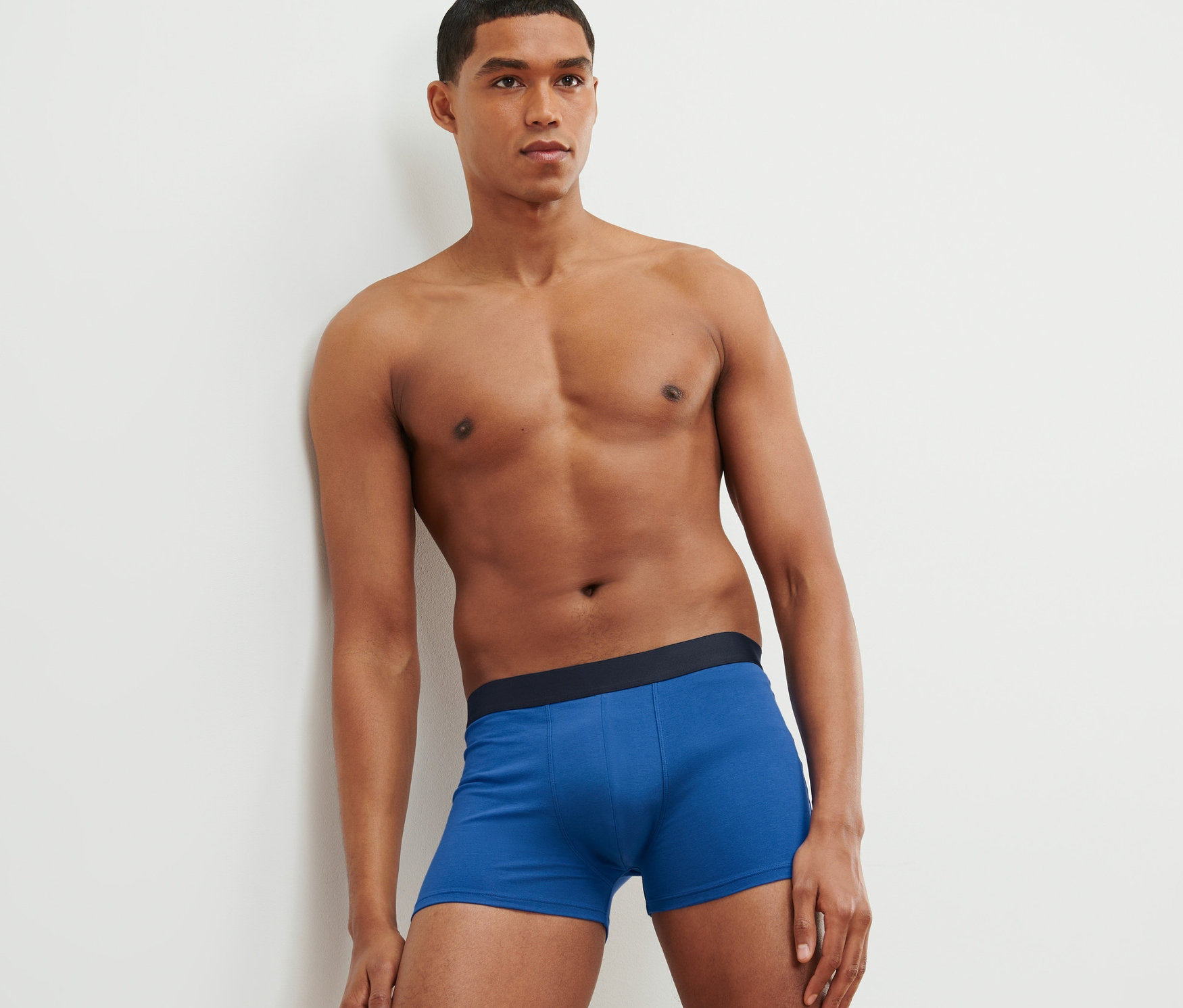 Un homme appuyé contre un mur portant 4 boxers, bleu, impression intégrale et gris.