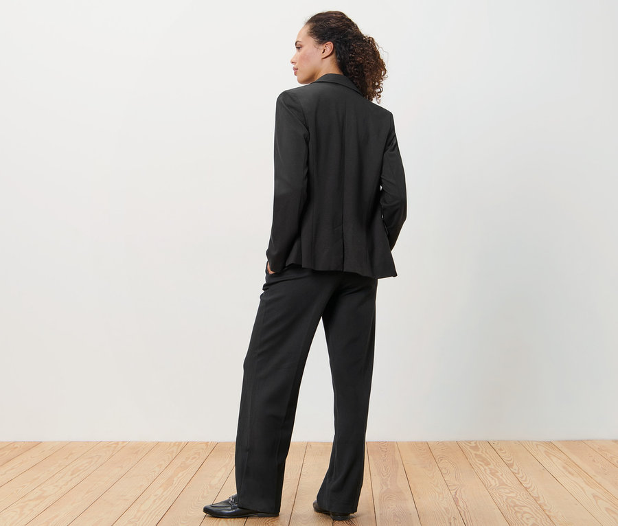 Femme portant un blazer en jersey noir et un pantalon, dos à la caméra.
