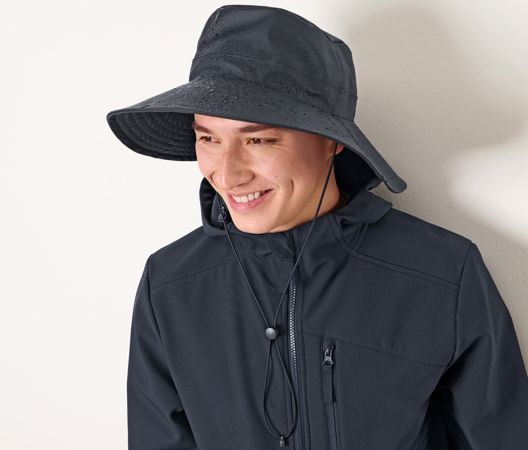 Homme souriant portant un chapeau de pluie bleu foncé et une veste.
