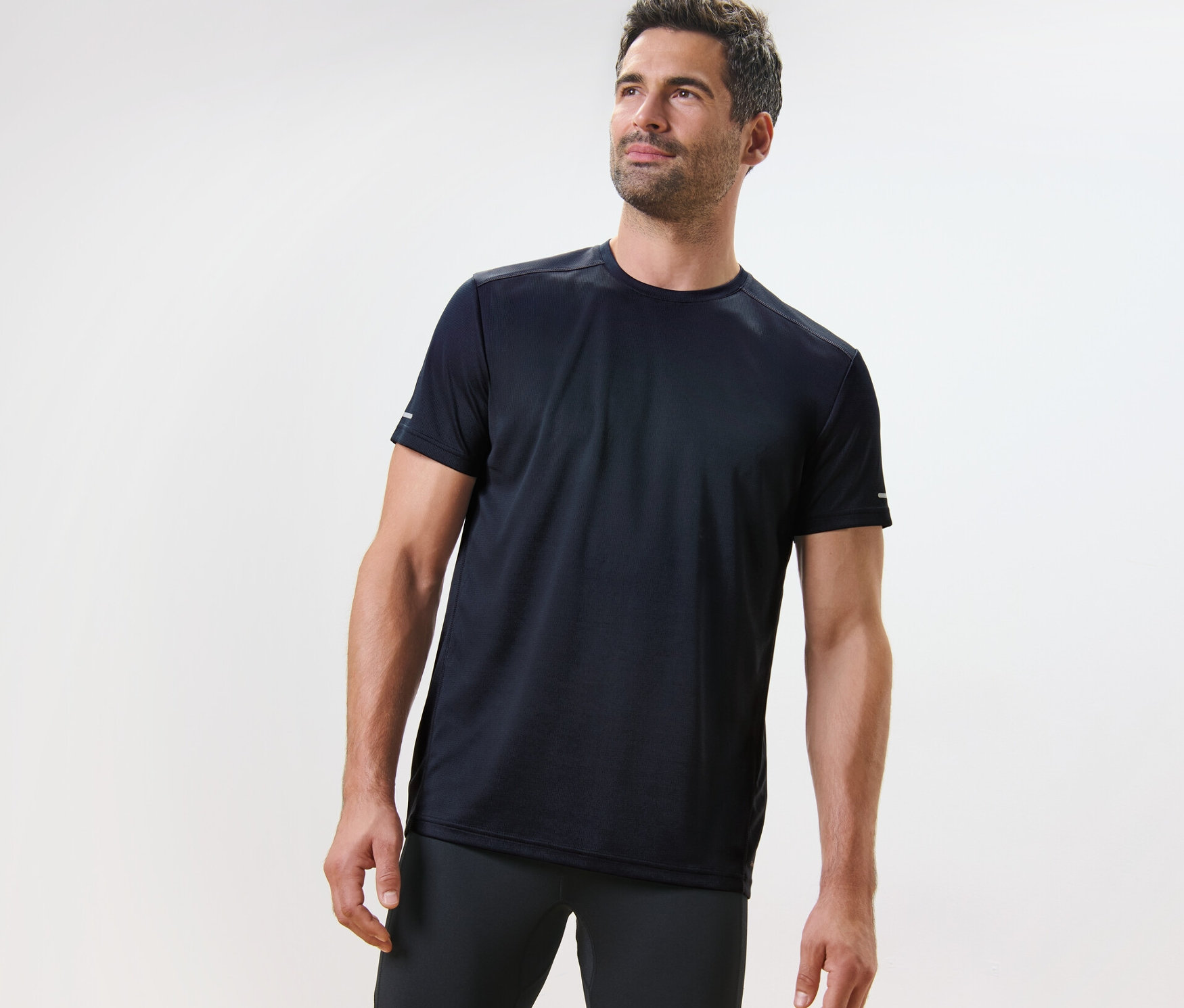 Un homme portant un t-shirt technique bleu marine se tient sur un fond clair.