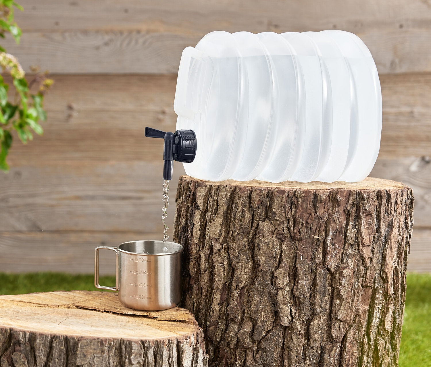 Un jerrican pliable est posé sur une souche d'arbre et verse de l'eau dans une tasse en métal.