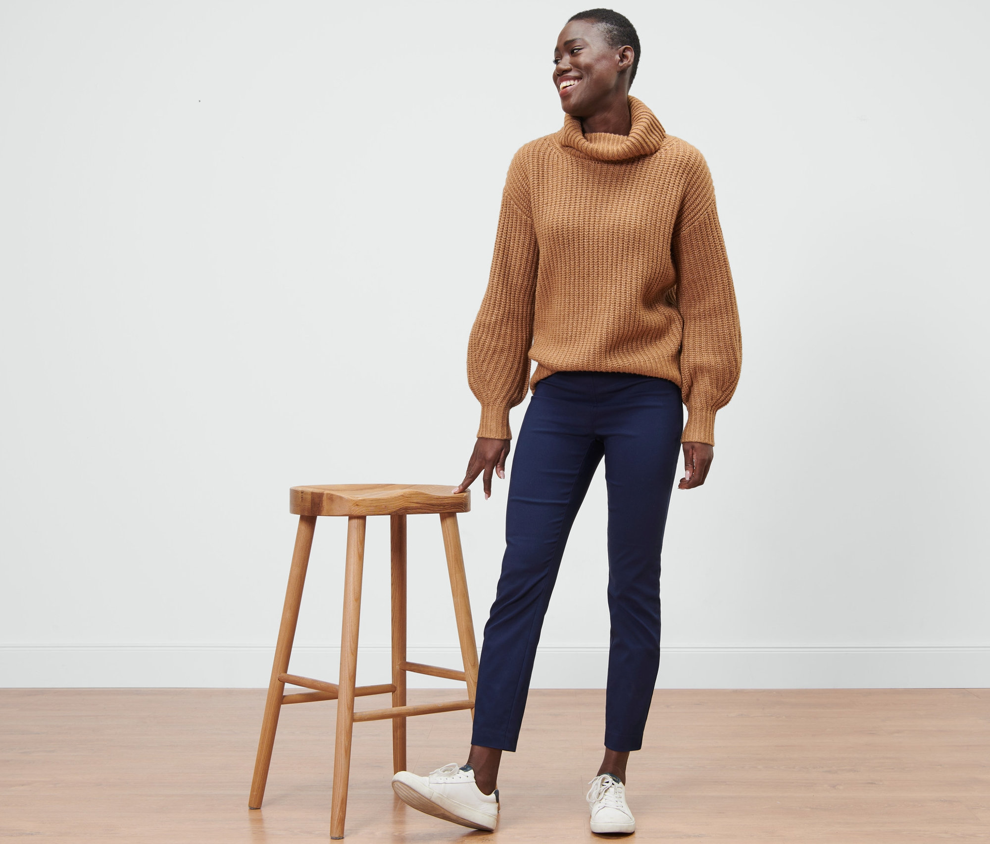 Une femme se tient à côté d'un tabouret en bois et porte un pantalon stretch bleu.
