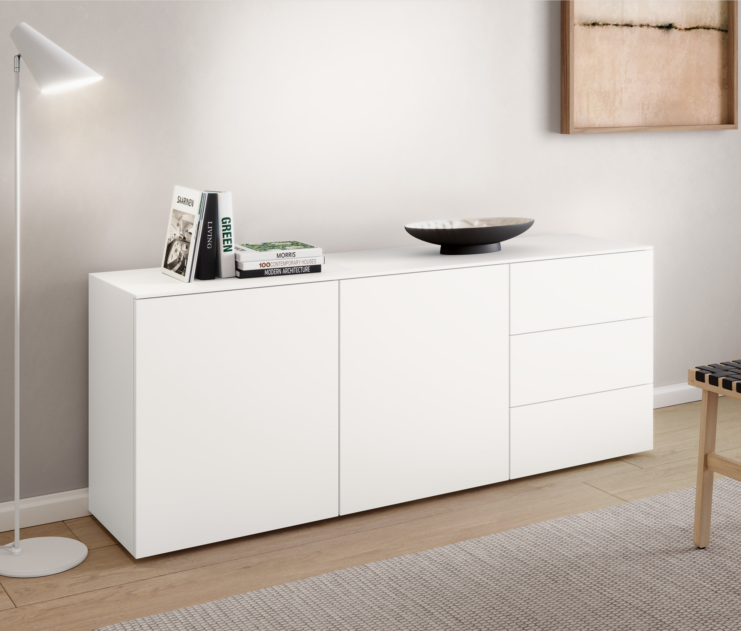 Un lampadaire en métal « Cale » blanc est placé à côté d'un buffet. Des livres et un bol sont posés sur le buffet. Un tabouret est placé à côté du buffet.