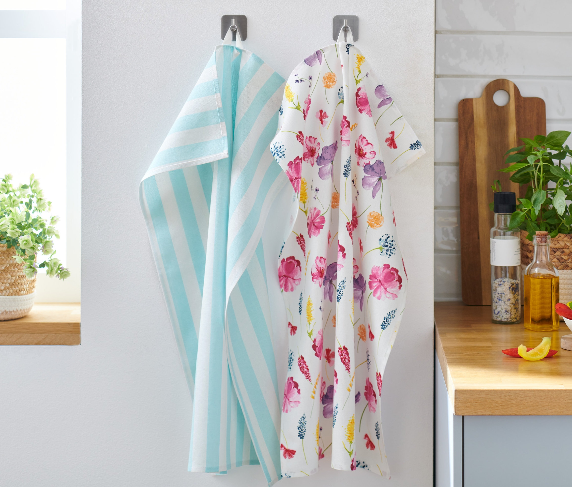 Deux torchons de cuisine sont accrochés au mur, un avec des rayures bleues et un avec un motif floral. Ce sont 2 linges de cuisine.